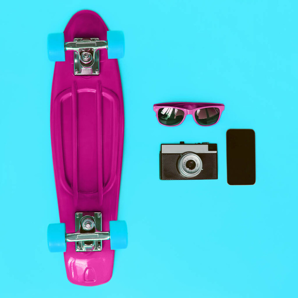 Colorful stylish set, vivid skateboard, sunglasses, vintage film camera and smartphone screen on a blue background, top view, flat lay - Foto, immagini