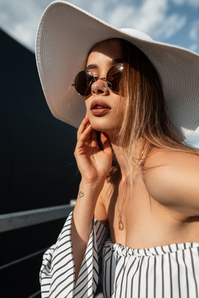 Lumoava malli nuori nainen seksikäs huulet olki hattu aurinkolasit muodikas raidallinen top poseeraa auringossa kaupungissa. Houkutteleva tyttö tyylikäs kesämekko nauttii rentouttava aurinkoisena päivänä. - Valokuva, kuva