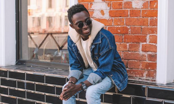 Portrait of stylish happy smiling young african man on a city street over brick wall background - Фото, изображение