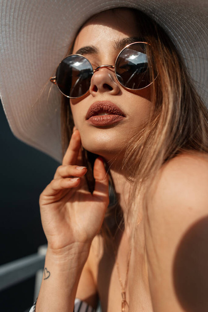 Vogue portrait young woman with clean health tanned skin with sexy lips in trendy round sunglasses in beautiful stylish striped blouse in straw vintage hat on sunny day. European girl model and sun. - Фото, изображение