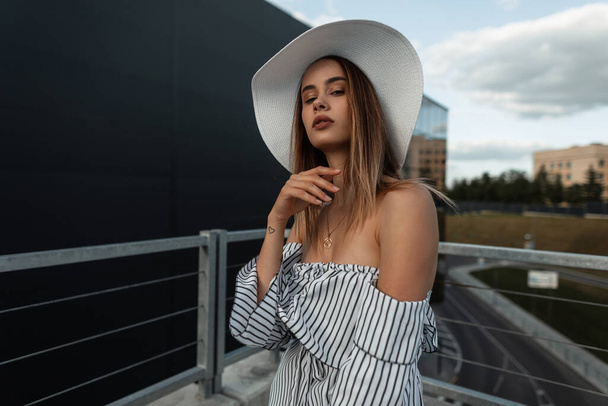 Μοντέρνο όμορφο κορίτσι μοντέλο με ένα χαριτωμένο πρόσωπο σε ένα μοντέρνο καπέλο με μια καλοκαιρινή κορυφή στο δρόμο. Γυναικεία αστική μόδα και στυλ ένδυσης - Φωτογραφία, εικόνα
