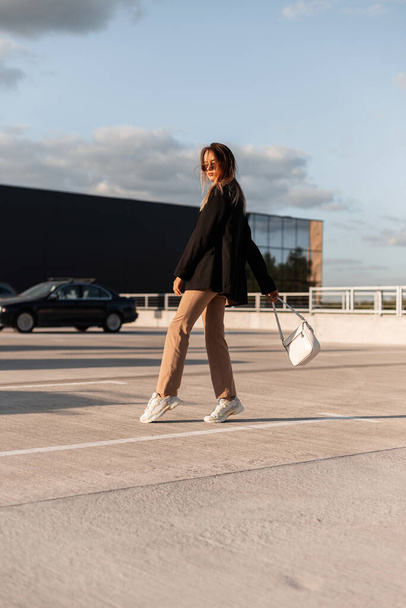 Urban trendikäs nuori nainen laukku tyylikäs rento vaatteita ja kenkiä kävelee ostoskeskukseen. Moderni tyttö poseeraa ulkona aurinkoisena kesäpäivänä. Tyylikäs ilme. - Valokuva, kuva