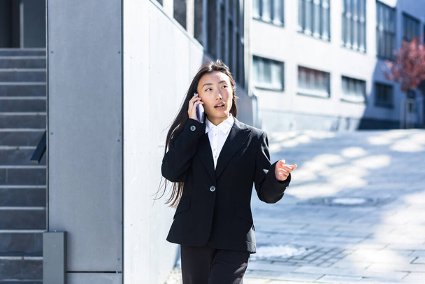 Beautiful Asian woman talking on the phone, business woman on a break walking near the office - Fotografie, Obrázek