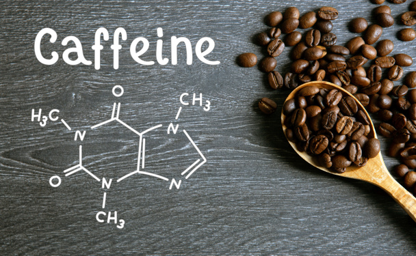 kávová zrna s dřevěnou lžící a chemickou strukturou kofeinu na dřevěném stole - Fotografie, Obrázek