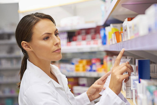 Tracking down prescriptions. Shot of an attractive young pharmacist checking stock in an aisle. - Photo, Image