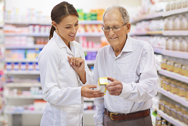 Die Fragen aus der Medikation herausnehmen. Aufnahme eines jungen Apothekers, der einem älteren Kunden hilft. - Foto, Bild