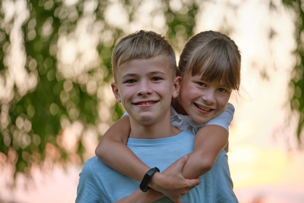 Happy siblings hugging lovingly in summer park. Young children brother and sister embracing each other outdoors. Family love and relationship concept - Photo, Image