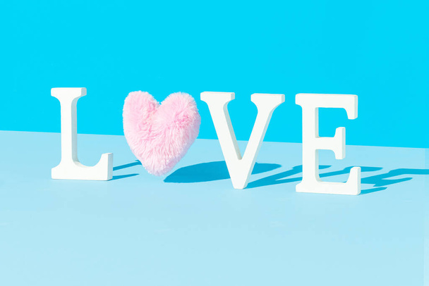 Minimales LIEBE-Wort aus weißen Buchstaben und zotteligem rosa Herz vor hellblauem Hintergrund. Trendiges Valentinskonzept. - Foto, Bild