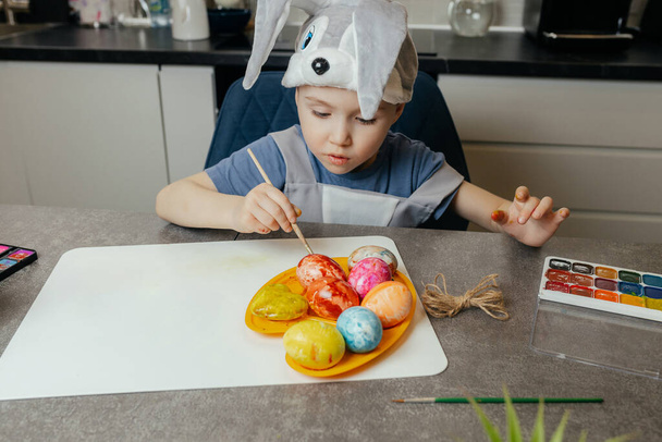 Lähikuva söpö viisivuotias pupu poika maalaus pääsiäismunia keittiössä. Loman käsite.  - Valokuva, kuva