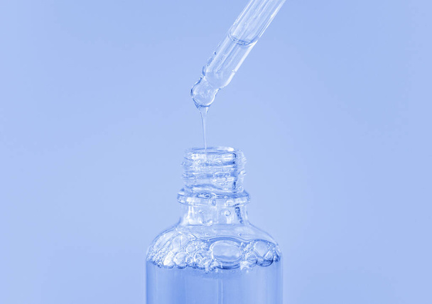 Pipeta z przezroczystym płynnym kwasem hialuronowym lub surowicą na niebieskim tle. Kosmetyki i koncepcja opieki zdrowotnej zbliżenie - Zdjęcie, obraz