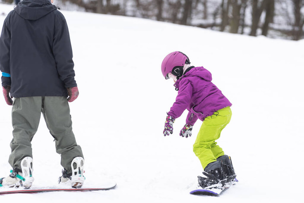 little cute girl learning to ride a childrens snowboard, winter sports for the child, safety of active sports. - Photo, Image