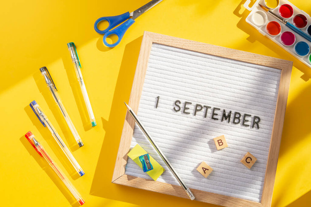 1 сентября письмо доска со школьными принадлежностями, как ручки, ножницы, ABC, краски на желтом фоне. Образование. День знаний, учеба, возвращение к школьной концепции - Фото, изображение