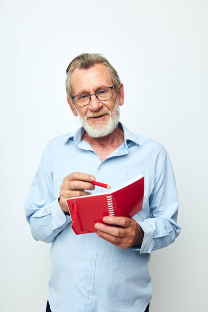 Portrait of happy senior man with red notebook and pen light background - 写真・画像