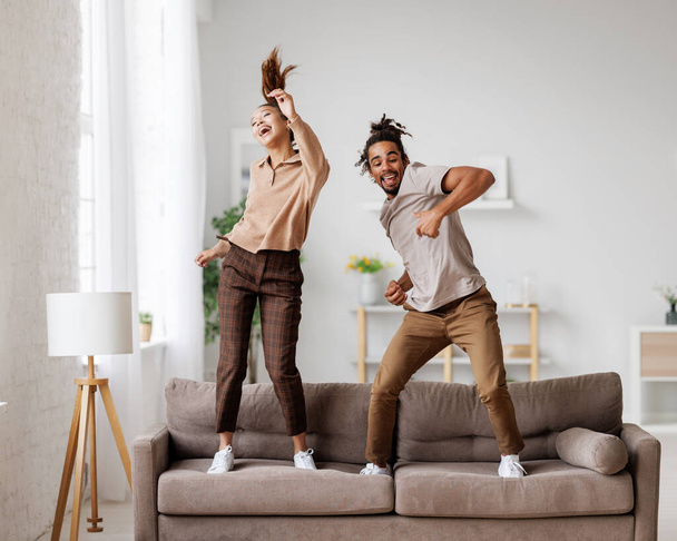 Young overjoyed african american family couple dancing to music on sofa at home - Foto, afbeelding