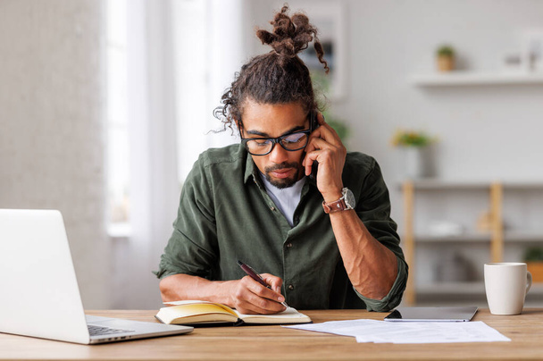 Mladí soustředěný muž podnikatel volat přes smartphone, zatímco pracuje vzdáleně z domova - Fotografie, Obrázek