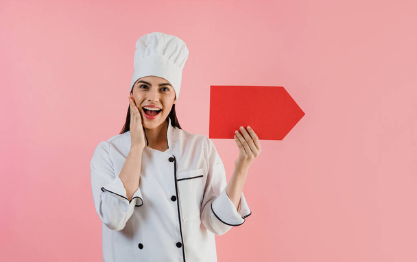 Portrait of young latin woman with chef hat holding a banner and copy space on a pink background in latin America - Photo, Image