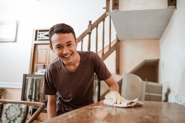 A boy smiles as he wipes a wooden cupboard - Φωτογραφία, εικόνα