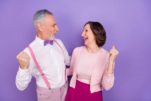 Portrait of two astonished successful aged people raise fists celebrate isolated on purple color background - Foto, Imagem