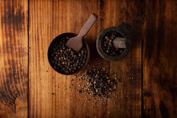 Black pepper in a small Molcajete (traditional Mexican version of the mortar and pestle) and small bowl on rustic wooden background. Top view - Foto, Bild