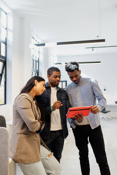 Latynoska i dwóch czarnych mężczyzn pracujących razem używając tabletu w biurze. przestrzeń współpracy. - Zdjęcie, obraz