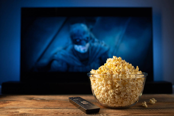 Een glazen kom van popcorn en afstandsbediening op de achtergrond de Tv werkt. 'S avonds gezellig kijken van een film of Tv-serie thuis. - Foto, afbeelding