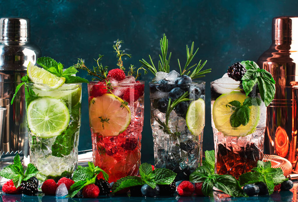 Cocktails or mocktails drinks. Classic summer refreshing long drink in highballs with berries, lime, herbs and ice on blue table background - Foto, immagini
