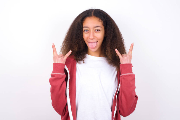 schönes Teenie-Mädchen in lässiger Kleidung, die vor weißem Hintergrund steht, Geste macht und Zunge zeigt - Foto, Bild