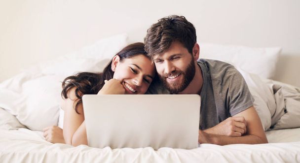 Risparmia tempo ogni giorno per connetterti. Girato di una giovane coppia felice utilizzando un computer portatile mentre si rilassa sul letto a casa. - Foto, immagini