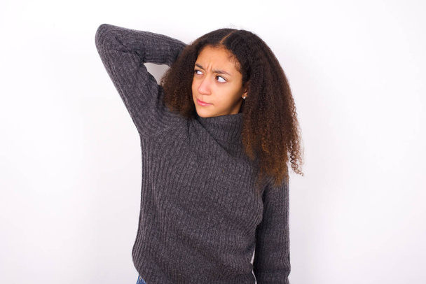 beautiful teen girl wearing grey turtleneck standing against white background confuse and wonder about question. Uncertain with doubt, thinking with hand on head. Pensive concept. - Photo, Image