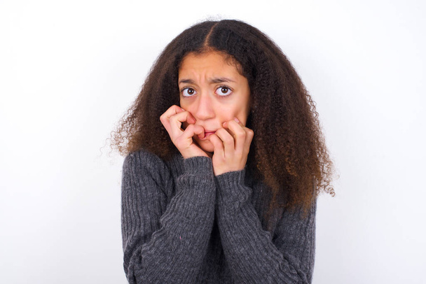 Angst mooie tiener meisje dragen grijze coltrui staan tegen witte achtergrond houdt handen dicht bij de mond, voelt bang en bang, heeft een fobie, Schok en angstig concept. - Foto, afbeelding