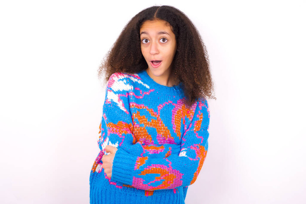 Shocked embarrassed beautiful teen girl wearing colorful sweater standing against white background keeps mouth widely opened. Hears unbelievable novelty stares in stupor - Photo, Image