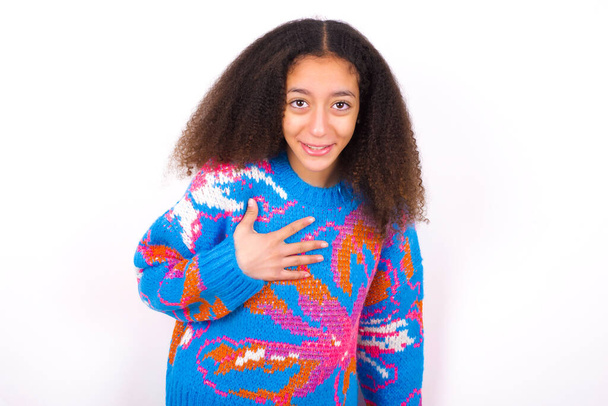 beautiful teen girl wearing colorful sweater standing against white background smiles toothily cannot believe eyes expresses good emotions and surprisement - Foto, Imagem