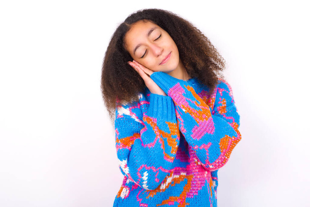 beautiful teen girl wearing colorful sweater standing against white background leans on pressed palms closes eyes and has pleasant smile dreams about something - Fotó, kép