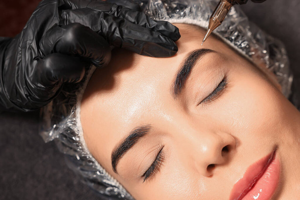 Young woman undergoing procedure of permanent eyebrow makeup in tattoo salon, top view - Photo, image