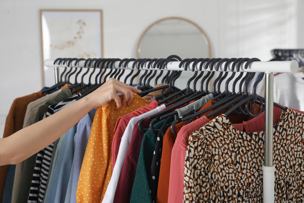 Woman picking clothes from rack indoors, closeup. Fast fashion - Photo, Image