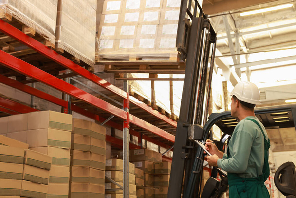 Worker near forklift truck with cardboard boxes in warehouse. Logistics concept - Φωτογραφία, εικόνα