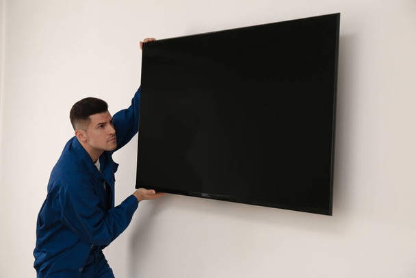 Professional technician installing modern flat screen TV on wall indoors - Zdjęcie, obraz