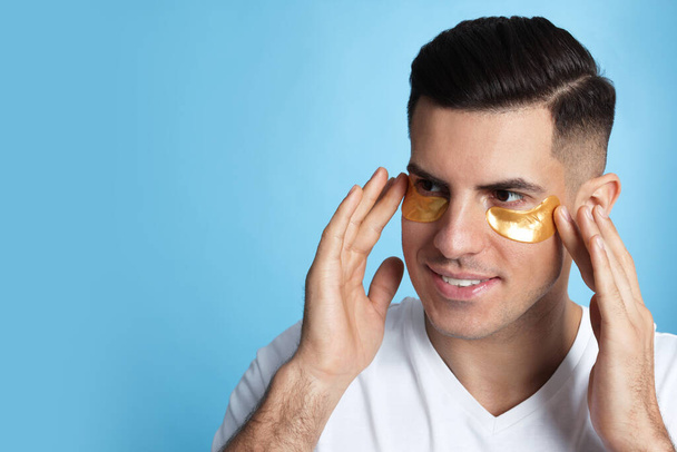 Man applying golden under eye patches on light blue background. Space for text - Photo, Image
