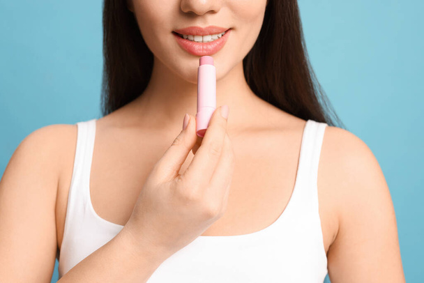 Young woman applying lip balm on turquoise background, closeup - Фото, изображение