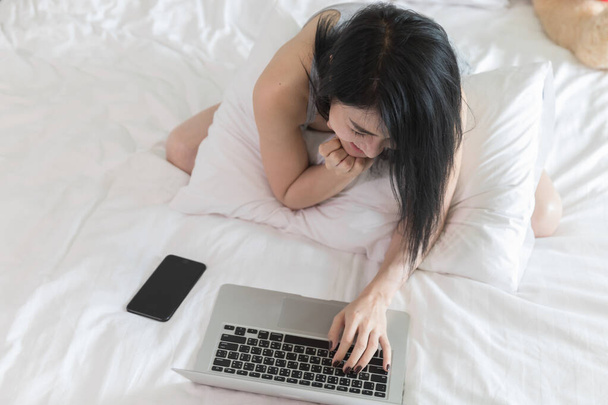 nő használ laptop fehér ágyon fehér hálószoba otthon topview fotó lágy fókusz sport - Fotó, kép