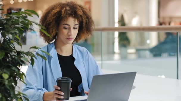 Fiatal komoly fókuszált millenniumi afro-amerikai lány üzleti nő szabadúszó menedzser szakember ül asztalnál kávézóban dolgozik laptop válaszol üzenetet ír jelentés tanulmány ivás kávé - Felvétel, videó
