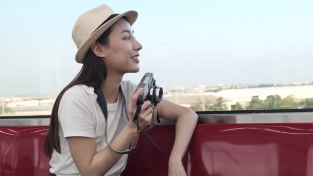 Gyönyörű ázsiai női turista fényképezőgéppel ül a piros ülés, utazik vonattal, hogy pillanatfelvétel fotó, amikor a közlekedés a külvárosban nézet, élvezze az utas életmód vasúton, boldog utazást nyaralást. - Felvétel, videó