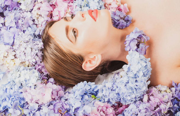 Beauty Woman lying on flowers. Blossom Makeup cosmetics and skincare. Girl with hydrangea flowers. - Fotó, kép