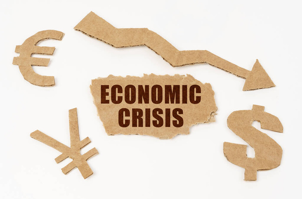 Economy and crisis concept. On a white background, dollar, euro and yen symbols, an arrow pointing down and a cardboard with the inscription - economic crisis - Foto, Bild