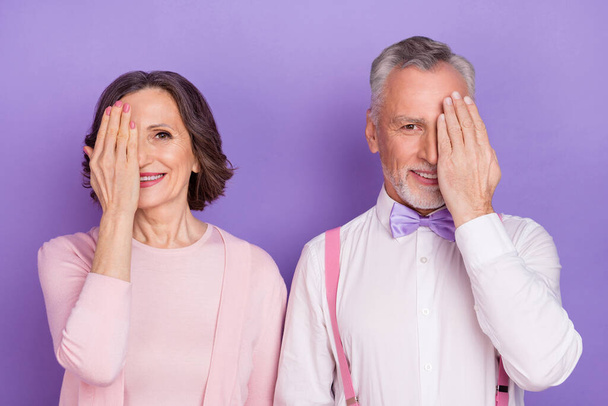 Portrait of two positive cheerful people arm palm cover eye look camera isolated on purple color background - Фото, изображение