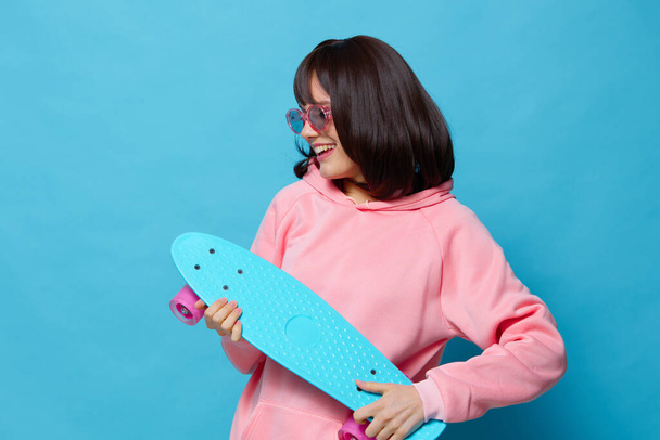 belle femme dans un pull rose skateboard divertissement fond bleu - Photo, image
