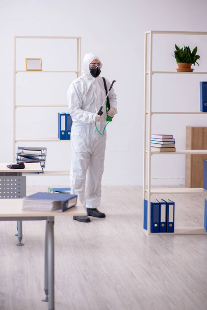 Jonge mannelijke contractant desinfecteert kantoor tijdens pandemie - Foto, afbeelding