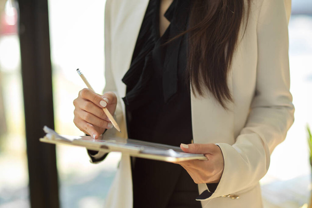 Cropped shot, Businesswoman standing in the office and holding a financial clipboard paperwork. - 写真・画像