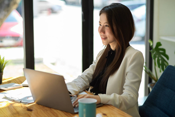 Gyönyörű ázsiai irodai hölgy vagy üzletasszony dolgozik a hordozható laptop a kávézóban.  - Fotó, kép