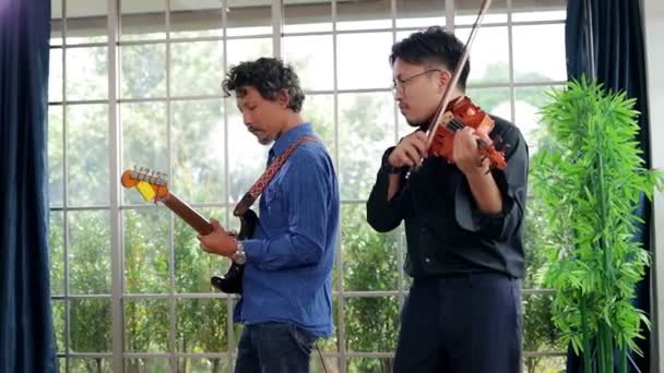 Két ázsiai férfi játszik együtt klasszikus hangszereken hegedűn és gitáron egy gyakorlóteremben. Mindketten szeretnek zenélni. Az élő zene és zenekarok lejátszásának fogalma - Felvétel, videó